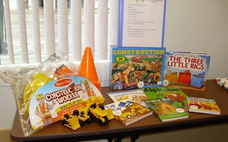 Contents of Play Early Literacy Kit including books, construction toys, and a construction worker dress-up set