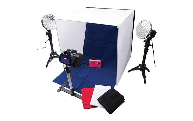 A camera on a stand photographing a small object against a blue backdrop with two lights shining on it